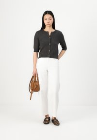 Gilet court gris foncé avec des manches courtes, fermeture à boutons, pantalon blanc à jambes larges, chaussures plates à imprimé animal, et sac à main marron.