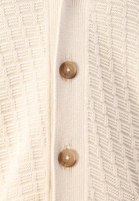Knitted beige cardigan featuring a textured pattern and two round brown buttons at the front, highlighting a cozy, refined design.
