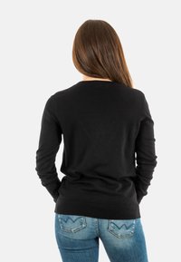 Jersey negro de manga larga con cuello redondo, combinado con unos jeans ajustados de color azul claro que presentan un sutil diseño de bolsillo trasero.