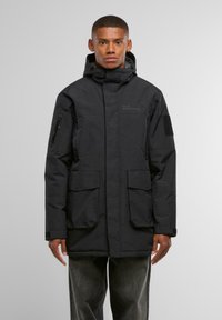 Černá parka s kapucí, obsahující dvě přední kapsy a kapsu s zipem na rukávu. Vyrobena z odolného, texturovaného materiálu.