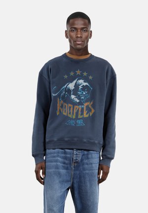 Sudadera azul marino con un estampado gráfico de pantera y el texto "Kooples". Presenta un cuello redondo, mangas largas y puños acanalados. Combinada con jeans de mezclilla clara.