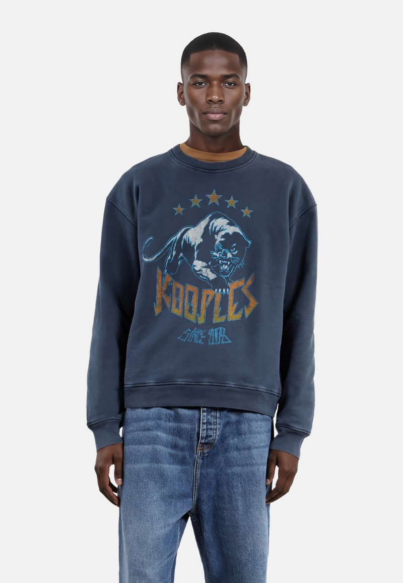 Marineblauwe sweatshirt met een grafische panterprint en "Kooples" tekst. Heeft een ronde hals, lange mouwen en geribbelde manchetten. G gedragen met een licht denim jeans.