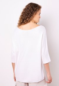 Weißer, locker sitzender Pullover mit weitem Halsausschnitt, Dreiviertelärmeln und einem strukturierten Strickmuster. Glatte Oberfläche.
