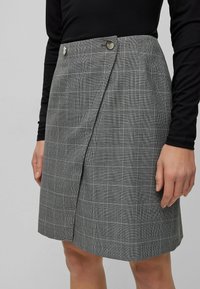Grijs geruit rokje met een wikkeldesign, twee zilverkleurige knopen in de taille en een gladde textuur.