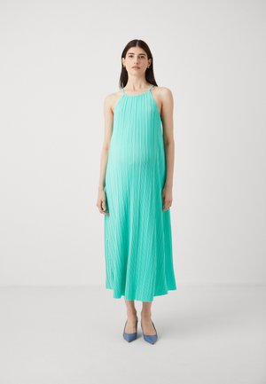 O rochie lungă, plisată, de culoare mentă strălucitoare, cu decolteu halter. Țesătura are o textură netedă, completată cu pantofi cu vârf ascuțit, de culoare albastră.