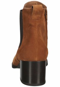 Bota de tobillo de ante marrón con punta redondeada, paneles laterales elásticos y tacón negro apilado. Presenta detalles de costura y una pestaña en la parte posterior para facilitar el calzado.