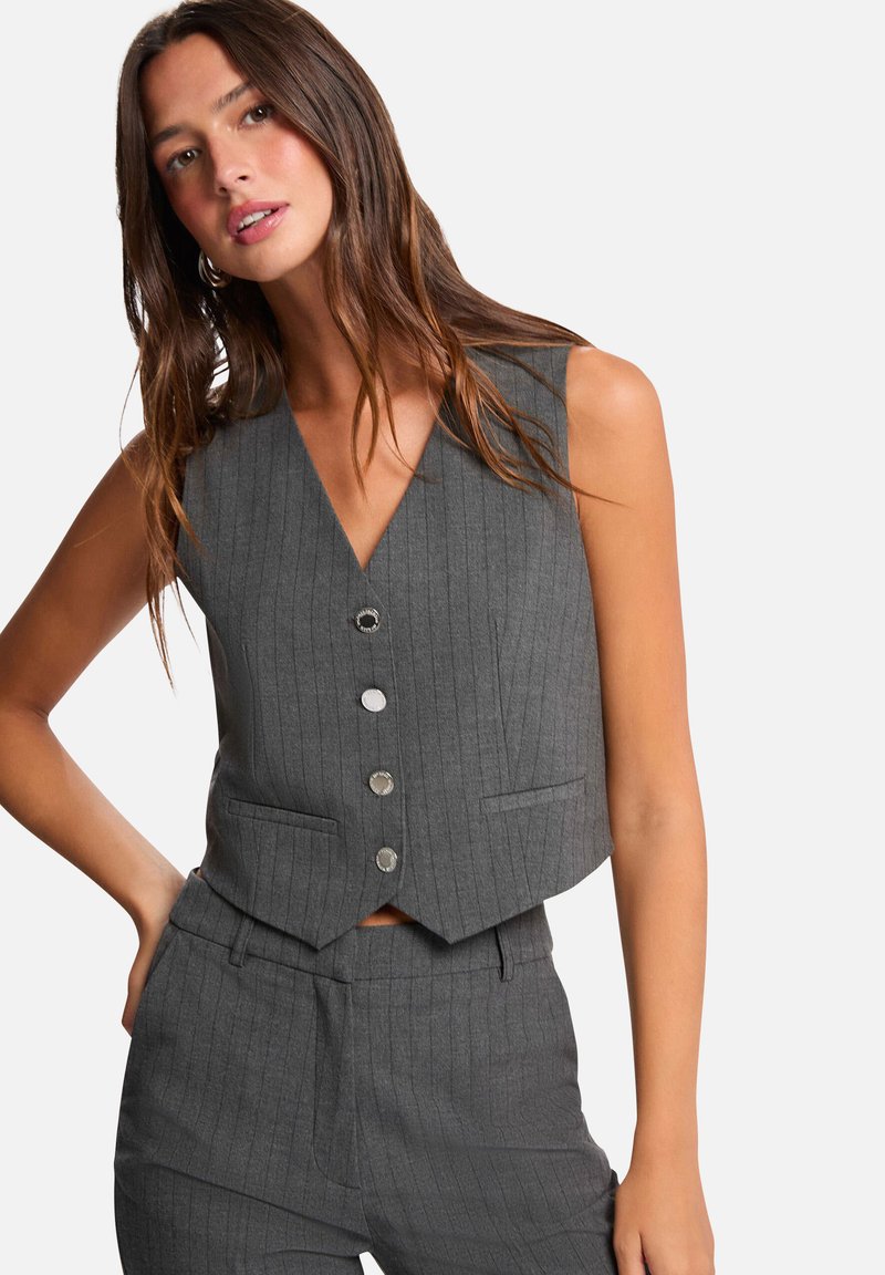 Gilet gris à rayures avec un décolleté en V profond, cinq boutons en argent et deux poches avant, fabriqué dans un tissu texturé.