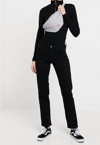 Un pull col roulé noir à côtes, un jean noir taille haute, un sac banane gris avec un logo rose, et des baskets noires avec des semelles blanches.