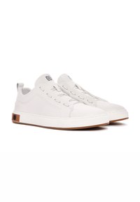 Zapatillas de piel blanca con una textura suave, suela de goma plana y acentos grises. Presentan cordones elásticos y un diseño minimalista.