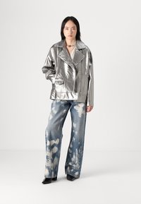 Sølvfarget faux skinnjakke med brede revers, glidelås og lomme. Kombinert med løse, slitte blå denimjeans med hvite mønstre.