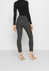 Black ribbed top paired with fitted, high-waisted plaid trousers in black, white, and grey. Strappy white heels complete the look.