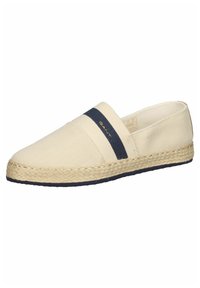 Beige canvas espadrill med ett marinblått randigt elastiskt band, jutesula och tvåfärgade accenter. Har en slät textur och en lätt på-och-av design.
