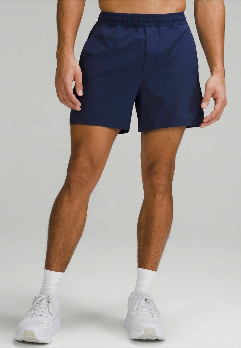 Marineblaue Sportshorts mit einem elastischen Bund, seitlichen Taschen und einem leichten Material, kombiniert mit weißen Turnschuhen und Socken.