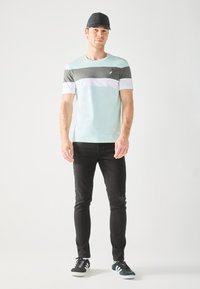 Vaaleansininen ja harmaa raidallinen t-paita lyhyillä hihoilla, yhdistettynä mustiin slim fit -farkkuihin, joissa on kulutettuja yksityiskohtia, sekä mustiin lenkkareihin.