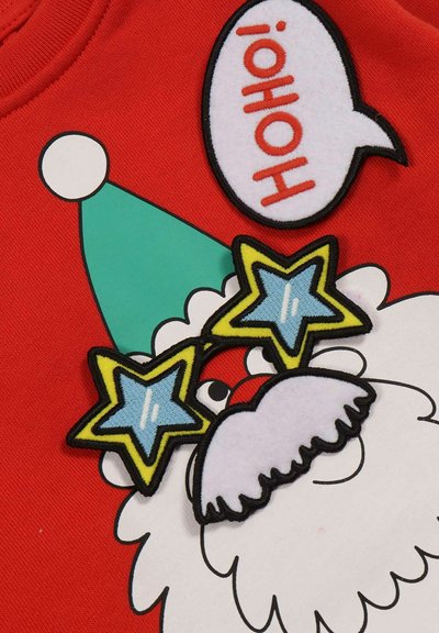 Święty Mikołaj w niebieskich, gwiazdkowych okularach i turkusowym kapeluszu na czerwonym tle z dymkiem mówiącym "HoHo!"