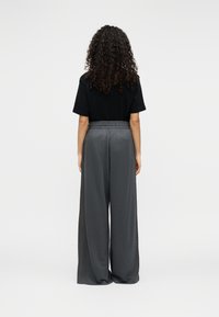 Μαύρη μπλούζα με κοντά μανίκια συνδυασμένη με γκρι παντελόνι φαρδιάς γραμμής. Το παντελόνι διαθέτει ελαστική μέση. Ομαλή υφή, άνετη εφαρμογή.