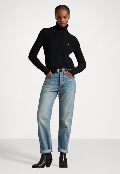 Svart kabelstickad polotröja, ljusblå raka jeans och svarta klackboots. Tröjan har en liten logotyp på bröstet.