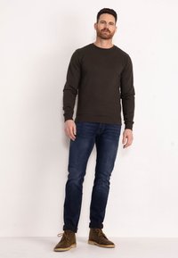 Dark green sweatshirt with long sleeves, crew neck, and ribbed cuffs, paired with blue jeans and brown suede ankle boots.