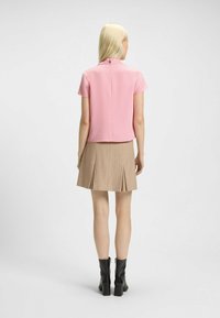 Top rosa corto con maniche corte e zip sul retro, abbinato a una gonna plissettata beige. Stivali neri con tacco completano il look.