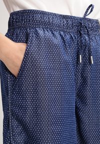 Navy siniset shortsit valkoisilla pilkuilla, joustava vyötärönauha, säädettävä nyöri ja sivutaskut, kevyestä kankaasta valmistettu.