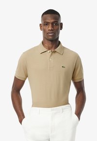 Beige pikétröja i bomullsblandning, kort ärm, med klassisk krage och tre knappar. Har en liten grön logga på bröstet.