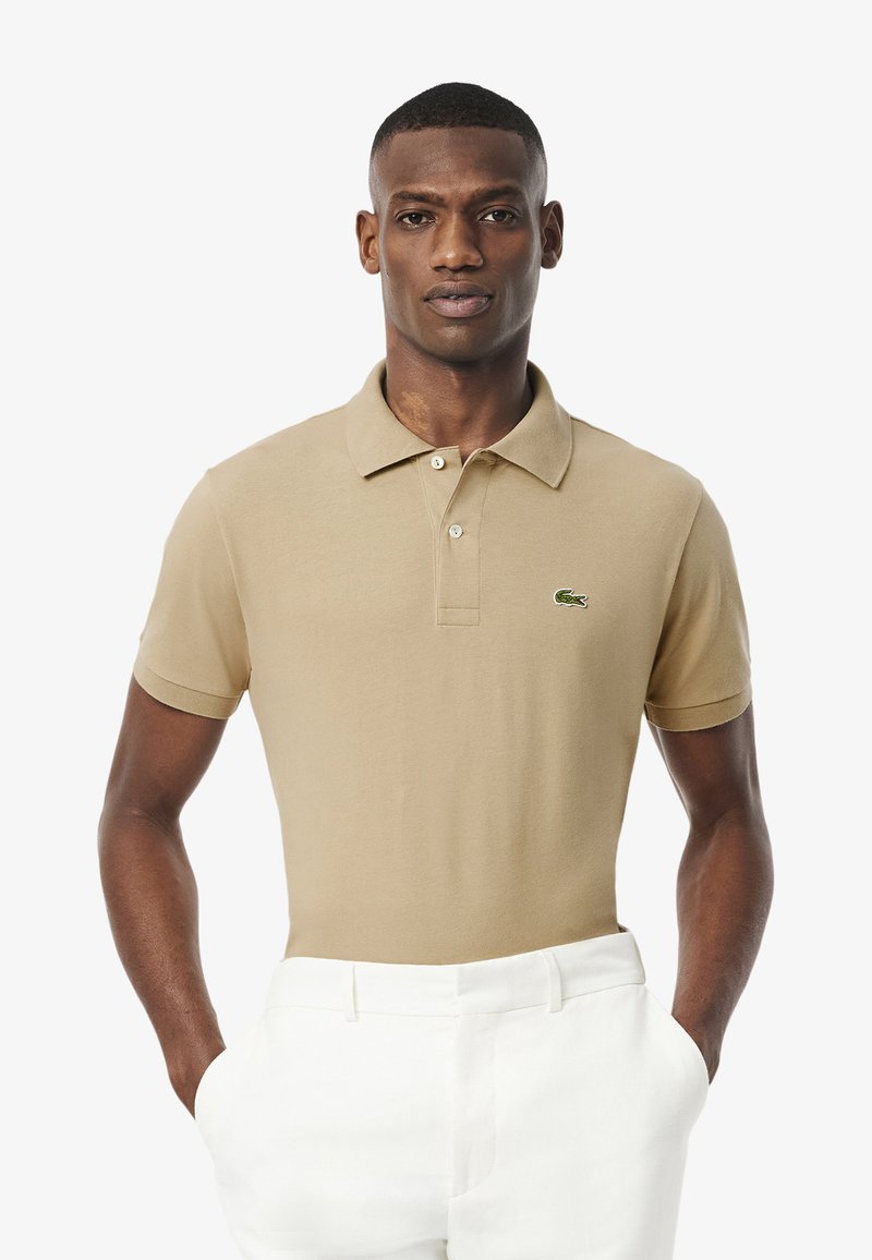 Beige pikétröja i bomullsblandning, kort ärm, med klassisk krage och tre knappar. Har en liten grön logga på bröstet.