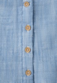 Tissu bleu clair texturé avec une rangée verticale de quatre boutons marron clair à quatre trous cousus au centre.