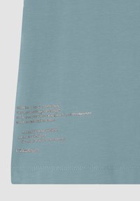 Camiseta de algodón azul claro con texto impreso en plata que detalla conceptos de bienestar y la marca 'FREDDY' en el lado inferior izquierdo.