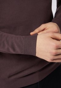 Strickpullover in Dunkelpurpur mit geripptem Bündchen und glatter Textur. Nahaufnahme von Händen, die den Ärmel zur Anpassung adjustieren.