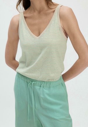 Mujer con top sin mangas de rayas verde claro con escote en V y pantalones anchos verdes menta con cordón, manos detrás de la espalda.