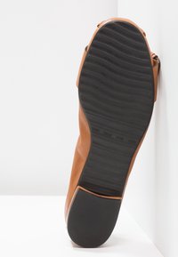 Chaussure plate en cuir marron avec semelle en caoutchouc noir montrant un motif de bande de roulement ondulé et talon carré, vue par dessous.