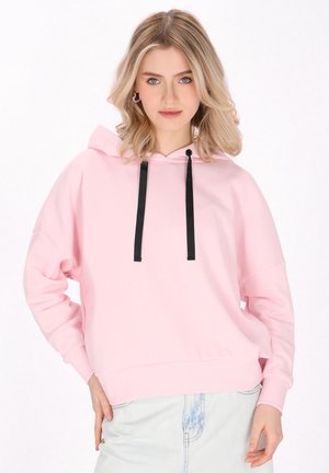 Sudadera con capucha rosa y cordones negros, de corte holgado y puños acanalados. Llevada con pantalones cortos de mezclilla claros, que poseen una textura suave.
