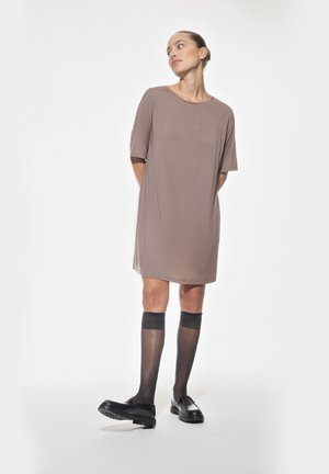 Kurzes, lockeres braunes Kleid aus glattem Stoff. Das Model trägt durchsichtige schwarze knielange Socken und klobige schwarze Loafers.