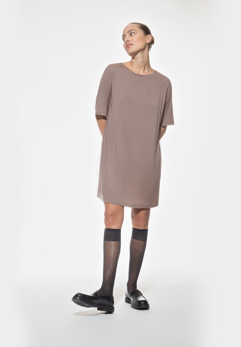 Robe brune à manches courtes, ample, en tissu lisse. Le modèle porte des chaussettes à genoux noires transparentes et des mocassins noirs épais.