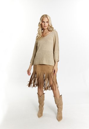 Beige pletený svetr s výstřihem do V a rukávy po tři čtvrtiny, doplněný hnědou sukní z semiše s dlouhými třásněmi. Hnědé kovbojské boty dotvářejí celý outfit.