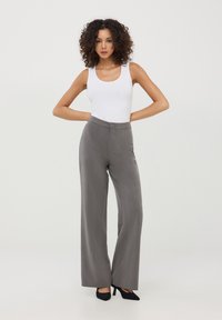 Pantaloni grigi a gamba larga con una texture liscia, dotati di chiusura frontale a bottoni e motivo a righe verticali. Abbinati a una canotta bianca aderente.
