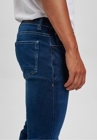 Mörkblå denimjeans med smal passform, sidfickor, kontrastsömmar och en strukturerad tygyta. Standard design på midjebandet.
