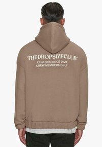 Light brown hooded sweatshirt with white text on the back. Features a relaxed fit, ribbed cuffs, and a wide waistband.