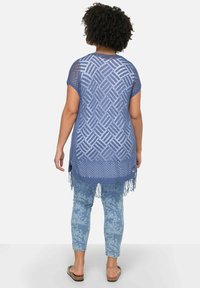 Tunic azzurra a maglia aperta con motivo a diamante, orlo a frange e maniche corte, abbinata a leggings floreali azzurri chiari. Sandali piatti.