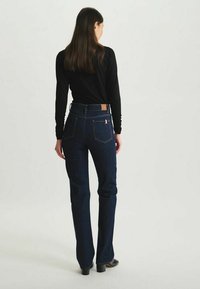 Jean évasés en denim bleu foncé avec une taille haute, dotés de poches arrière et d'une étiquette en cuir brun sur la ceinture arrière.