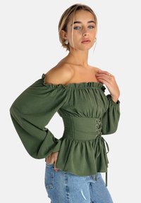 Olive green off-the-shoulder blouse with puff sleeves, ruched bodice, and lace-up detailing. Worn with light blue jeans, showcasing a relaxed fit.