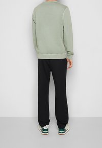 Ljusgrön sweatshirt med rund halsringning, ribbade muddar och nederkant, i kombination med svarta joggers och vita sneakers med gröna accenter.