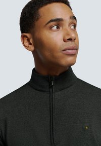 Donkergroen quarter-zip pullover van textiel met een gestructureerde stof, voorzien van een hoge kraag en een klein hexagonaal logo op de linkerkant van de borst.