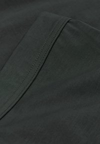 Donkergroene stof met een gladde textuur en zichtbare stiknaden. Het materiaal lijkt licht en flexibel, met een subtiele glans.