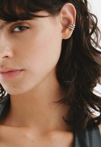 Pendiente de oreja de plata que presenta múltiples bandas apiladas con un acabado pulido, adornado con pequeños acentos circulares. Superficie suave y diseño elegante.