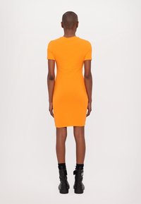 Orangetäckad klänning med korta ärmar och rund halsringning, som når till mitten av låret. Bärs med svarta ankelstövlar.