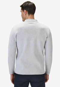 Grå långärmad polo i ett texturerat tyg, med en liten krage och en avslappnad passform, visad bakifrån.