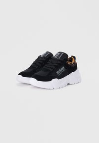 Sorte semskede sneakers med en hvit chunky såle. Har en svart tunge, lisser, sidelog og et mønstrete helldetalj.