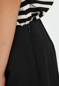 Falda negra con una textura suave y un cierre lateral oculto, combinada con una blusa a rayas en blanco y negro. Primer plano de los detalles de la costura lateral.