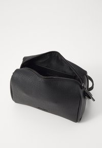 Sac en cuir noir texturé avec fermeture éclair, de forme ovale, et détail de marque à l'intérieur. Design compact adapté aux essentiels.